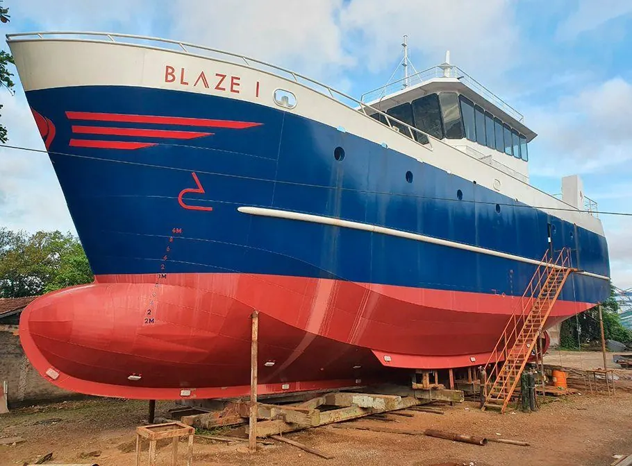 Embarcação Blaze I no estaleiro, casco azul com fundo vermelho e superestrutura clara